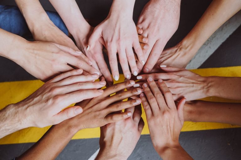 Hände greifen gemeinsam in die Mitte – Symbol für Teamwork