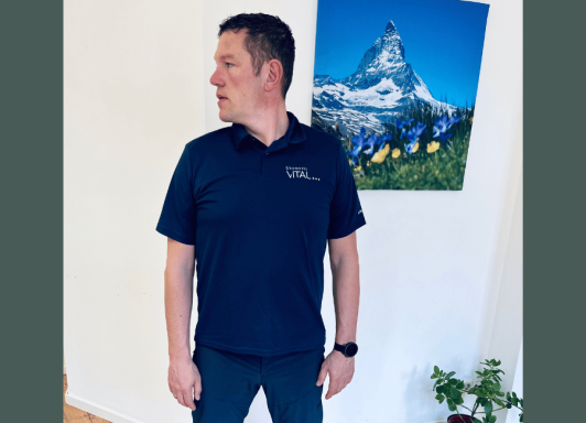 Ein Mann steht aufrecht und führt eine Nackenmobilisationsübung zur rechten Seite durch. 